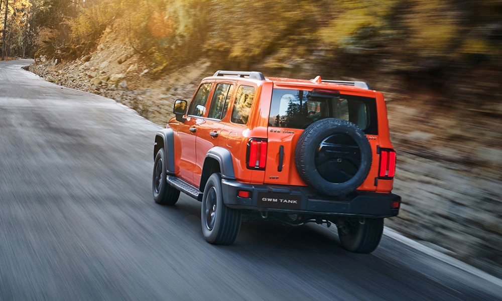 Vista trasera de camioneta SUV todoterreno Tank 300 color naranja siendo conducida por carretera con fondo de montañas.