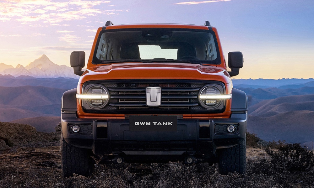 Vista frontal de camioneta SUV todoterreno Tank 300 color naranja con luces led y fondo de montañas.