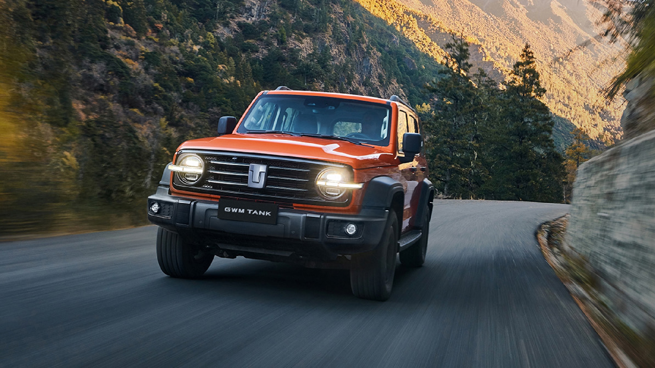Camioneta SUV todoterreno Tank 300 color naranja siendo conducida por carretera con fondo de montañas. 